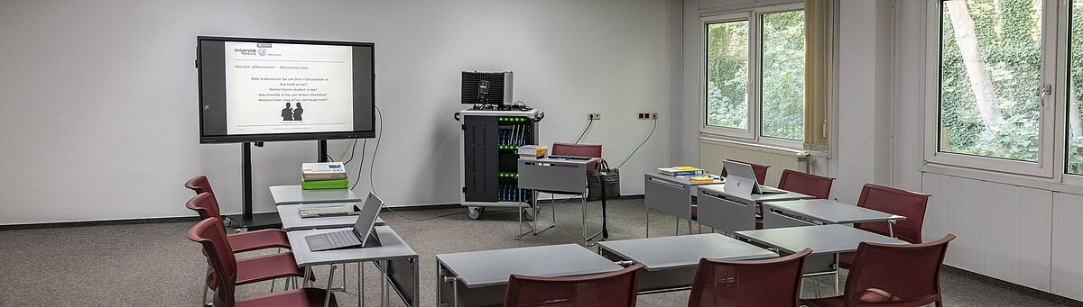 Ansicht Lehr-Lern-Raum der UB mit elektronischer Tafel, Tischen und Stühlen.