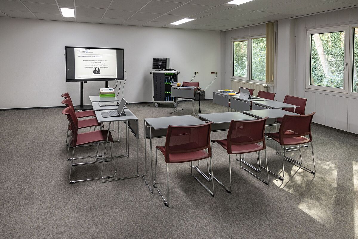 Ansicht Lehr-Lern-Raum der UB mit elektronischer Tafel, Tischen und Stühlen.